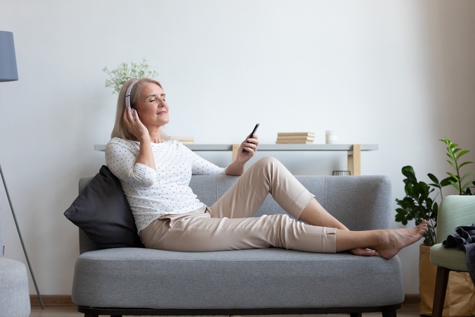 Seniorin mit Headset und Smartphone auf einem Sofa