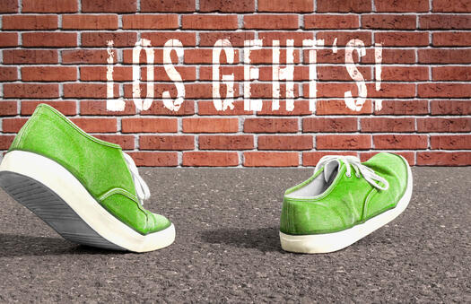 Zwei grüne Turnschuhe gehen auf eine Ziegelwand zu, auf der Los geht's steht